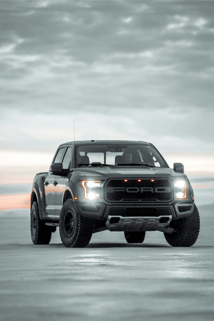 Grey Ford F150 Raptor with LED headlights on salt flat at dusk