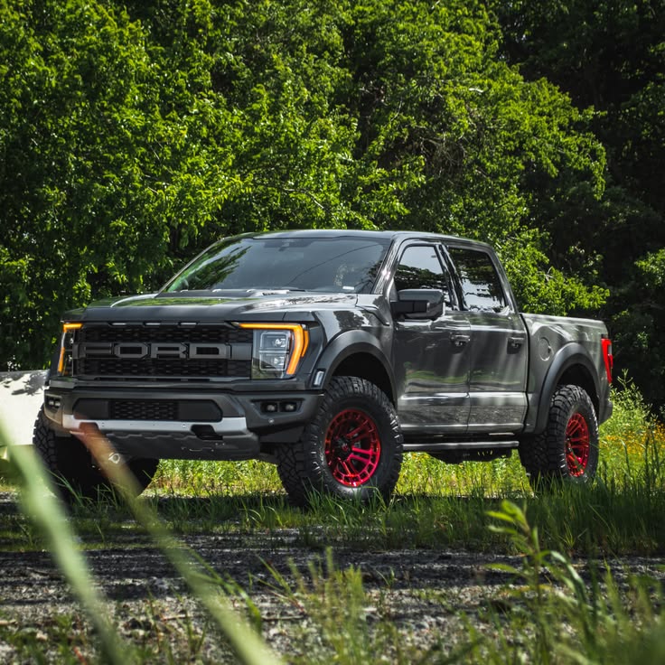 Black Ford F150 Raptor R lifted truck in forest with red wheels